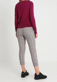 Fuksjowy sweter z długim rękawem w połączeniu z szarymi spodniami w kratkę do kostek oraz czarnymi trampkami z złotymi guzikami akcentującymi. Miękka dzianina i dopasowany krój.