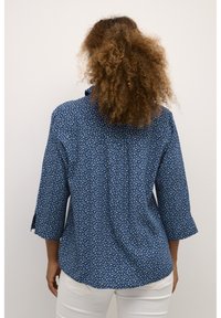 Chemise bleue à motif avec des manches trois-quarts, présentant un design floral en bleu clair et blanc sur un fond navy.