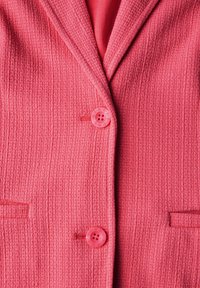 Różowa marynarka z teksturowanym wzorem, z dwoma okrągłymi guzikami i dwoma kieszeniami. Wewnętrzna podszewka majednolity różowy kolor.