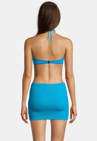 Haut de bikini en tricot bleu avec liens noués autour du cou, et mini-jupe assortie. La texture est côtelée, avec un design simple et une couleur unie éclatante.