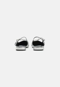 Silver metallic sandals with ankle straps, open back, flat soles, and a smooth texture. Minimal hardware detail on the straps.