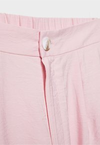 Gros plan sur un pantalon en tissu rose clair avec une ceinture élastique et une fermeture à bouton blanc à l'avant.