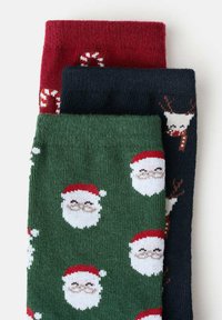 Tri páry vianočných ponožiek: červené s motívom cukrovej trstiny, zelené s tvárami Santa Clausa a námornícke modré so vzorom jeleňa. Mäkký pletený materiál.