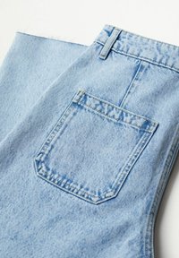 Jean en denim bleu clair plié, montrant la poche arrière et les passants de ceinture avec une couture détaillée sur un fond blanc.