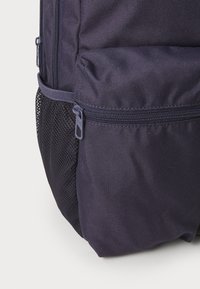 Mochila de un oscuro azul marino con tela texturizada, que cuenta con un bolsillo con cremallera y un panel lateral de malla. Los acentos de cremallera robusta añaden un detalle funcional.
