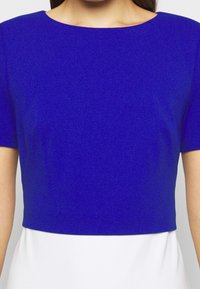 Krótki top w intensywnym kobaltowym kolorze, z krótkimi rękawami i okrągłym dekoltem, charakteryzujący się gładką fakturą i prostym wzornictwem.