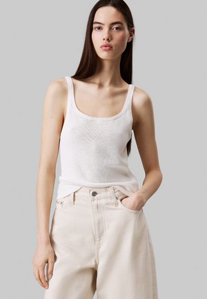 Débardeur en tricot blanc avec un décolleté carré, associé à un jean large beige taille haute. Texture lisse et coupe décontractée.