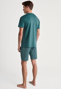 Aqua-kleurige katoenen t-shirt met korte mouwen, gecombineerd met een zwembroek met een patroon van een spiraalontwerp in het wit op een donkerblauwe achtergrond.