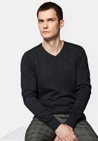 Ciemnoszary, dzianinowy sweter z dekoltem w serek, z długimi rękawami i ściągaczami, z delikatnym logo marki na klatce piersiowej.