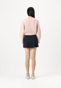 Light pink fuzzy sweater with long sleeves, paired with a dark pleated skirt and beige block-heeled shoes. The background is white.