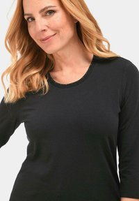 Zwart lang mouwenshirt met een ronde halslijn, voorzien van een gerimpelde rand en versieringen langs de rand. Zachte, gladde stof.