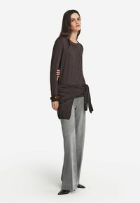 Mörkgrå långärmad topp med en knuten midjedetalj, matchad med ljusgrå vida byxor och spetsiga svarta skor. Slät textur.