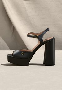 Μαύρο σανδάλι πλατφόρμα με χοντρό ψηλό τακούνι, λουράκι στον αστράγαλο με χρυσή αγκράφα και μικρή χρυσή καρδιά στη μπροστινή λουρά.