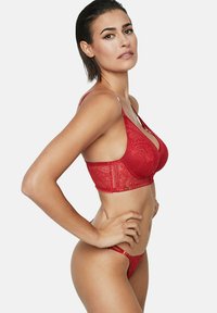 Soutien-gorge en dentelle rouge avec un motif décoratif, bretelles ajustables et un string assorti en dentelle rouge. Présente des textures transparentes et des détails complexes.
