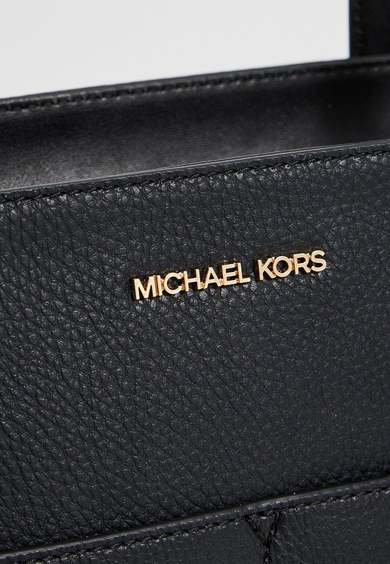 Zwarte leren handtas met textuur en een gouden "MICHAEL KORS" logo. Beschikt over ingewikkelde stiksels en een gestructureerd ontwerp voor duurzaamheid.