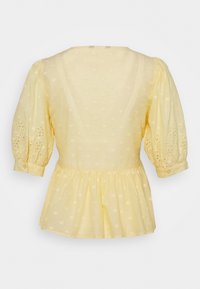Hellgelbe Bluse mit aufgebauschten Dreiviertelärmeln, Lochstickerei auf den Ärmeln, strukturierten Punkten und gerafftem Peplumsaum an der Taille.
