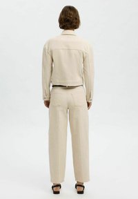 Chaqueta de mezclilla beige y pantalones de pierna ancha, tejido texturizado, diseño recortado, cierres abotonados, dos bolsillos traseros, combinados con sandalias negras.