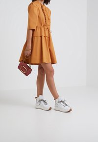 Musztardowa sukienka o krótkim rękawie z falbanami i z możliwością regulacji w pasie. Noszona z białymi trampkami za kostkę i małą bordową torebką.