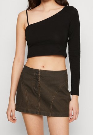 Top corto negro de un solo hombro con manga larga; combinado con una falda vaquera marrón que presenta costuras curvas y pespuntes en contraste.