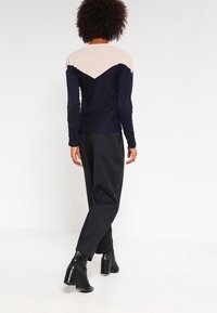 Långärmad topp med en marinblå kropp och beige axelpanel, i kombination med högmidjade, strukturerade svarta byxor och klackiga stövletter.