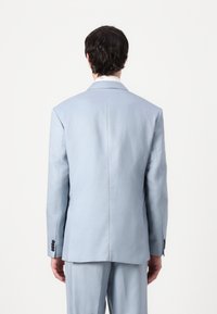 Chaqueta de traje azul claro con una textura suave, solapas con muesca y cuatro botones negros en cada puño. Ajuste entallado mostrado desde la parte de atrás.