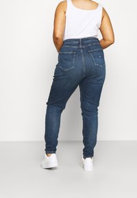 Mörkblå högmidjade jeans med smal passform, design med fem fickor och subtila sömdetaljer. Kombinerade med vita sneakers.