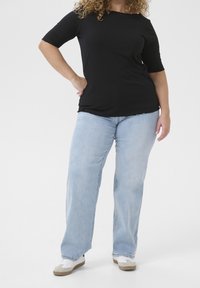 Schwarzes, geripptes Oberteil mit kurzen Ärmeln, kombiniert mit hellblauen, weiten Jeans und weißen Sneakers mit braunen Sohlen. Einfaches Design, keine Muster.