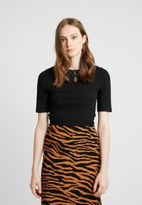 Schwarzes Kurzarmoberteil kombiniert mit einem braun-orangenen gestreiften Rock mit einem Tigerstreifenmuster. Einfache Schmuckakzente sind enthalten.