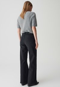 Maglione grigio, morbido, a maniche corte abbinato a jeans neri a vita alta e svasati. Tasche posteriori notevoli e calzature nere eleganti.