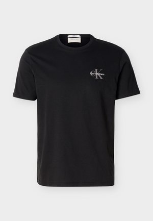 Μαύρο T-shirt με κοντό μανίκι και στρογγυλή λαιμόκοψη, με μικρό γκρι λογότυπο "CK" της Calvin Klein και λευκό κείμενο στην αριστερή πλευρά του στήθους.