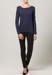 Marineblauw shirt met lange mouwen en een ronde hals, voorzien van accenten op de schouders en een nauwsluitend ontwerp. Gecombineerd met zwarte skinny jeans en hakken.