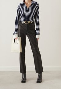 Gestreept marineblauw en wit langemouwen top, zwarte leren broek, robuuste zwarte haklaarzen en een crèmekleurige handtas met een uitsnijding in het handvat.