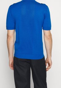 Modrá pletená polokošile s krátkými rukávy a jednobarevným předním dílem, zadní panel s texturovaným vzorem. Má žebrovaný límec a manžety.