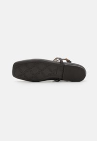 Semelle plate noire de sandale avec motif géométrique antidérapant et petit talon bloc, vue de dessous sur fond blanc.
