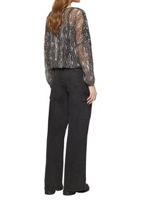 Blouse transparente à imprimé serpent noir et gris avec des manches longues, associée à un pantalon cargo noir taille haute avec des poches sur les côtés.