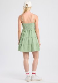 Vihreä ruudullinen kesämekko, jossa on säädettävät spagettiolkaimet, smockattu bodice, kerrokselliset röyhelöt ja levenevä helma, yhdistettynä valkoisiin lenkkareihin ja raidallisiin sukkiin.