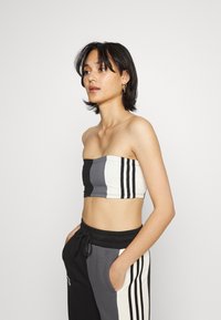 Bandeau crop top v čiernej, sivej a bielej farbe s vertikálnymi pruhmi; nosený so sivými teplákmi s povrazom a bočnými vreckami.