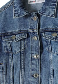 Veste en denim bleu clair avec des éléments en métal argenté. Elle dispose d'une fermeture à snaps, de deux poches poitrine et de coutures contrastées. Surface texturée.