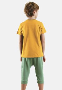 Gul kortærmet bomulds T-shirt parret med lysegrønne, cropped joggerbukser med sidelommer og ribbede manchetter.