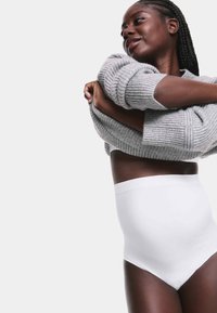 Hoge taille witte onderbroek van een gladde, rekbare stof, gecombineerd met een gezellige, lichtgrijze geribbelde trui, comfortabel gedragen.