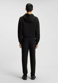 Schwarz Hoodie und Jogginghose Set aus weichem Stoff. Der Hoodie hat eine Kapuze mit Kordelzug, während die Jogginghose eine Gesäßtasche hat.