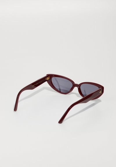 Lunettes de soleil cat-eye bordeaux avec des verres sombres, une monture en plastique lisse et des accents en métal doré sur les côtés.