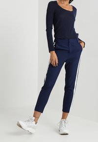 Marinblå figursydda byxor med vita sidostreck, tillverkade av ett mjukt tyg. Matchas med en marinblå långärmad topp och vita träningsskor.