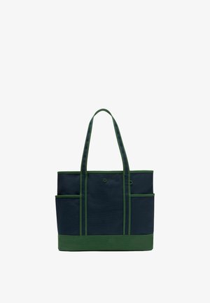 Marineblaue und grüne Tasche mit zwei langen Henkeln, seitlichen Außentaschen und einem kleinen runden Logo auf dem vorderen Mittelpaneel.