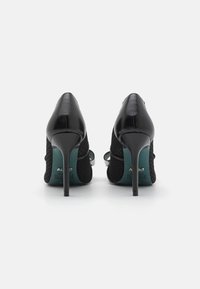 Chaussures à talons hauts noires avec une tige en mesh texturé, un bout pointu et un talon stiletto élégant. Semelle intérieure verte avec un détail de marque visible.