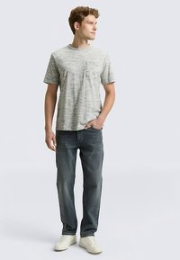 Vaaleanharmaa, raidallinen lyhythihainen t-paita taskulla, yhdistetty tummansinisiin farkkuihin ja valkoisiin lenkkareihin. Yksinkertainen, rento malli.