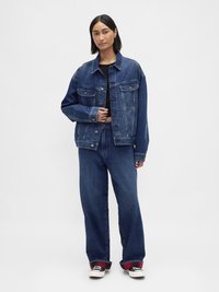 Denimjakke med to brystlommer, knappestengning og løs passform. Kombinert med vide denimjeans og svarte joggesko med røde detaljer.