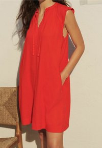 Rode mouwloze jurk met een losse pasvorm, met een halslijn met strikjes en zijzakken. Zachte stof met een lichte textuur.