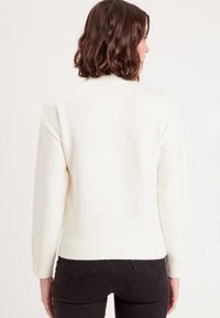 Pull crème en maille douce, avec un col montant, des épaules abaissées et des poignets et ourlet côtelés.