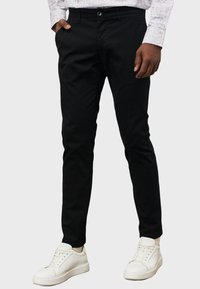 Pantaloni slim-fit neri realizzati in un mix di cotone, con tasche e zip, abbinati a sneakers bianche per un contrasto.
